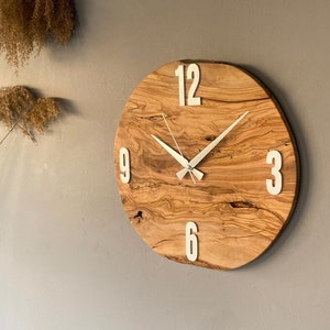 May include: A round wooden clock with white numbers and hands. The clock has a natural wood grain pattern.