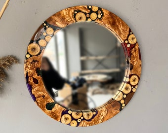 May include: Round mirror with a wooden frame featuring a unique design of colorful resin and wood pieces. The frame is made of natural wood with a variety of colors and textures.