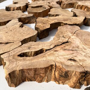 May include: A collection of natural wood slices, each with unique grain patterns and textures. The slices are various sizes and shapes, with some having a rough, bark-like edge. The wood is a light brown color with darker brown streaks.
