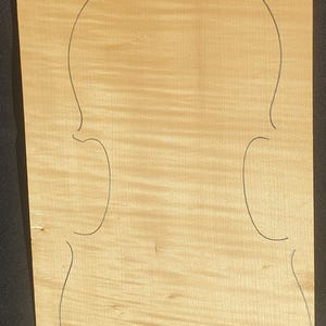 Puede incluir: Una tapa de violín de madera clara con un contorno oscuro de la forma del violín. La madera tiene un veteado natural. El texto "1PB - 248" está impreso en la esquina superior izquierda.