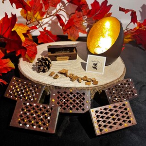Peut inclure: Cinq petites boîtes en bois avec des motifs complexes et des accents dorés et blancs. Les boîtes sont disposées sur une surface en bois avec une petite pomme de pin et un bougeoir doré. Le bougeoir est sur une surface en bois avec une petite pancarte qui dit "Moments & Tea".