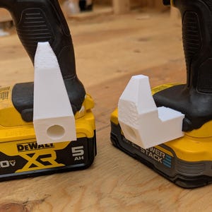 May include: Two white 3D-printed drill attachments are mounted on yellow and black cordless drills. The drills have black handles and are labeled "DeWALT" and "POWER STACK". The attachments have a cylindrical hole.
