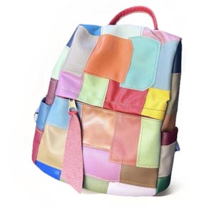 May include: A colorful patchwork leather backpack with a top handle and a front zippered pocket. The bag features a variety of colors, including red, blue, green, yellow, and pink. The zipper pull has a pink tassel.