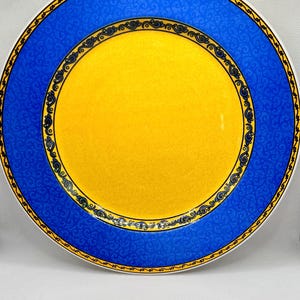 May include: A decorative plate with a vibrant design. The plate features a bright yellow center, a wide blue border with a swirling pattern, and a gold and black decorative trim. The plate is a round shape.