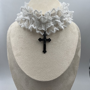 May include: White lace choker with a black cross pendant.