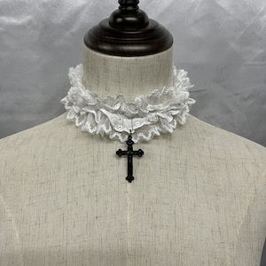 May include: A white lace choker with a black cross pendant. The choker is made of delicate lace and has a ruffled edge. The cross pendant is simple and elegant.