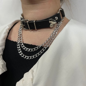Puede incluir: Un collar de cuero negro con un dije de corazón plateado y dos cadenas plateadas.