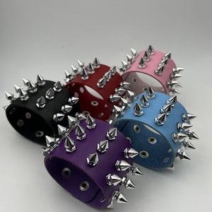 May include: Five leather bracelets with silver pyramid-shaped studs. The bracelets are in black, red, light blue, purple, and pink.