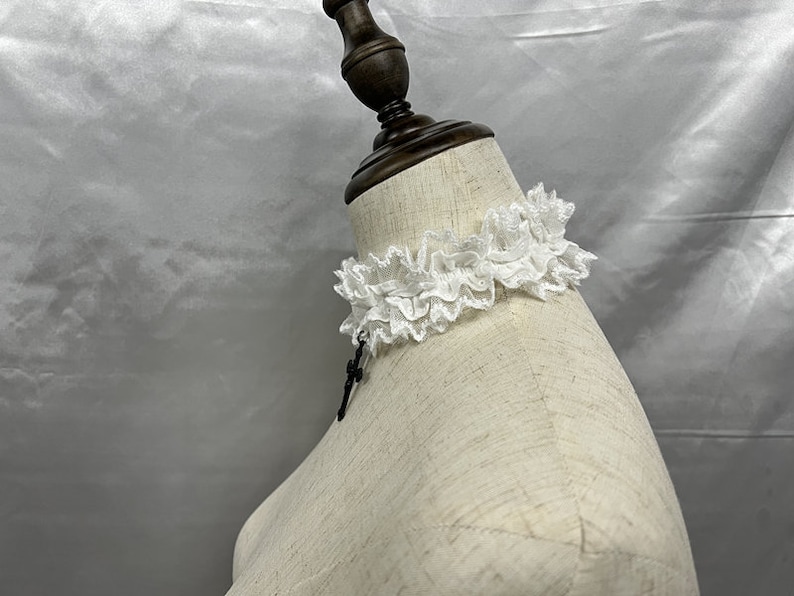 May include: White lace choker with a black pendant on a white mannequin.