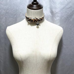 May include: A brown and black leopard print choker with a silver heart charm.