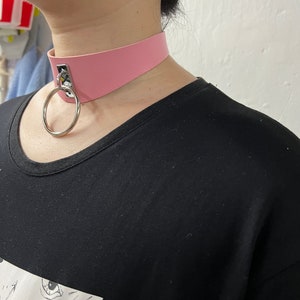 May include: A pink faux leather choker with a silver ring and a silver clasp.