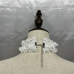 May include: White lace choker necklace with a silver chain and clasp. The choker is on a white mannequin bust.