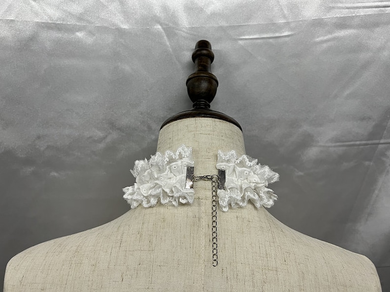 May include: White lace choker necklace with a silver chain and clasp. The choker is on a white mannequin bust.