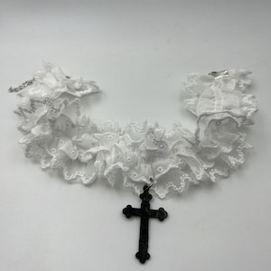 May include: White lace choker necklace with a black cross pendant.