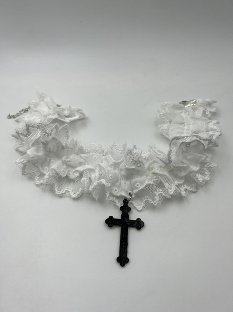 May include: White lace choker necklace with a black cross pendant.