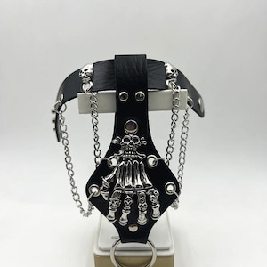 May include: Black leather wrist cuff with a silver skull hand design, studded with silver rivets and adorned with silver chains.