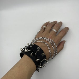 May include: A black leather wrist cuff with silver metal spikes and a silver chain attached.