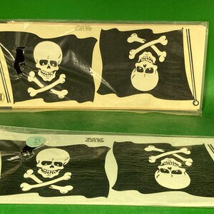 May include: Two packages of pirate flag decals. Each flag is black with a white skull and crossbones design. The decals are rectangular and packaged in clear plastic.