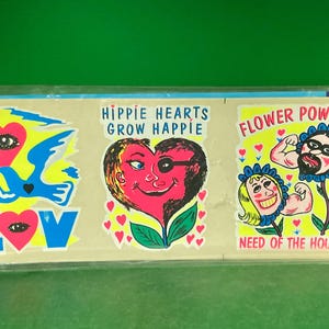 May include: A sheet of vintage stickers with a retro hippie theme. Designs include a heart with an eye, a dove, the word "LOVE", a heart with an eye patch, and the phrases "Hippie Hearts Grow Happie" and "Flower Power".