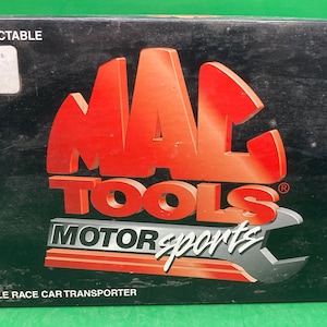 May include: A black box with a red and white Mac Tools Motorsports logo. The box is labeled "Adult Collectable" and "1:64 Scale Race Car Transporter".