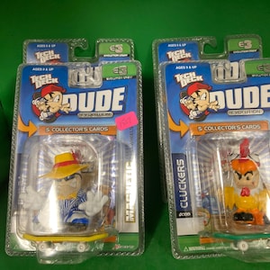 May include: Two Tech Deck Dude Evolution skateboards in clear plastic packaging. One features a character in a yellow hat and blue striped shirt. The other has a chicken character. Each package includes 5 collector's cards.