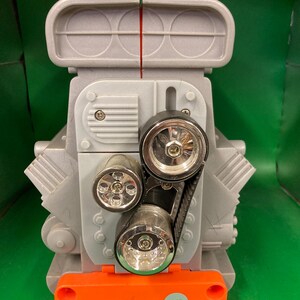 May include: A gray toy engine with a black belt, silver accents, and an orange base. The engine has three circular lights and a rectangular top. The number "1480" is printed on the orange base.