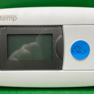 May include: White thermostat with a digital display and a blue sticker that says "667". The thermostat has buttons for heat, off, cool, fan, on, and auto.