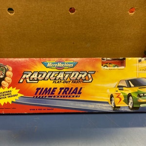 May include: A Micro Machines Radiators Time Trial Speed Challenge toy set with a green and yellow race car, a finish line, and a digital stopwatch. The box features the text "Radiators Flat-Out Fast!" and "Over 6 Feet of Track!"