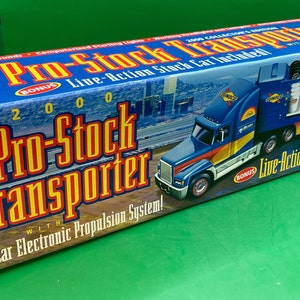May include: A blue and yellow toy semi-truck with a Sunoco logo and the text "Pro-Stock Transporter" on the side. The truck is carrying a blue and yellow race car with the text "Sunoco" on the side. The box also says "2000 Collection Edition" and "Live-Action Stock Car Included".