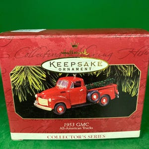 May include: A red Hallmark Keepsake ornament of a 1953 GMC All-American truck. The truck has a Christmas tree in the bed and is displayed in a red box with gold lettering. The box reads "Collector's Series."