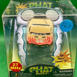 May include: A toy remote control car in a clear plastic package. The car is a yellow Chevy Camaro SS with red flames on the side. The package includes a remote control and the text "PHAT boyz" on the front. The package also includes the text "27 MHz" and "NO. 1847".