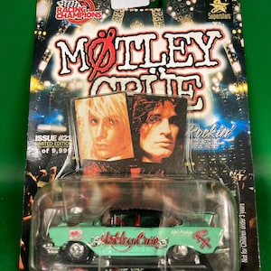 May include: A mint green die-cast model car with the text "Motley Crue" on the side, packaged on a card with the band's logo and images of band members. The packaging includes the text "Racing Champions" and "Adult Collectible".