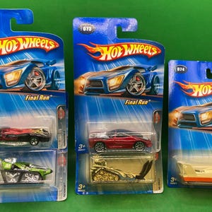 May include: Three Hot Wheels toy car packages with blue backgrounds and the words "Hot Wheels" and "Final Run" printed on them. Each package features a different toy car, including a red sports car, a black sports car, and a yellow construction vehicle.