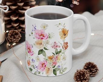 May include: White ceramic mug with a floral design featuring pink, yellow, and orange flowers. The mug is filled with a dark liquid and has a handle on the right side.