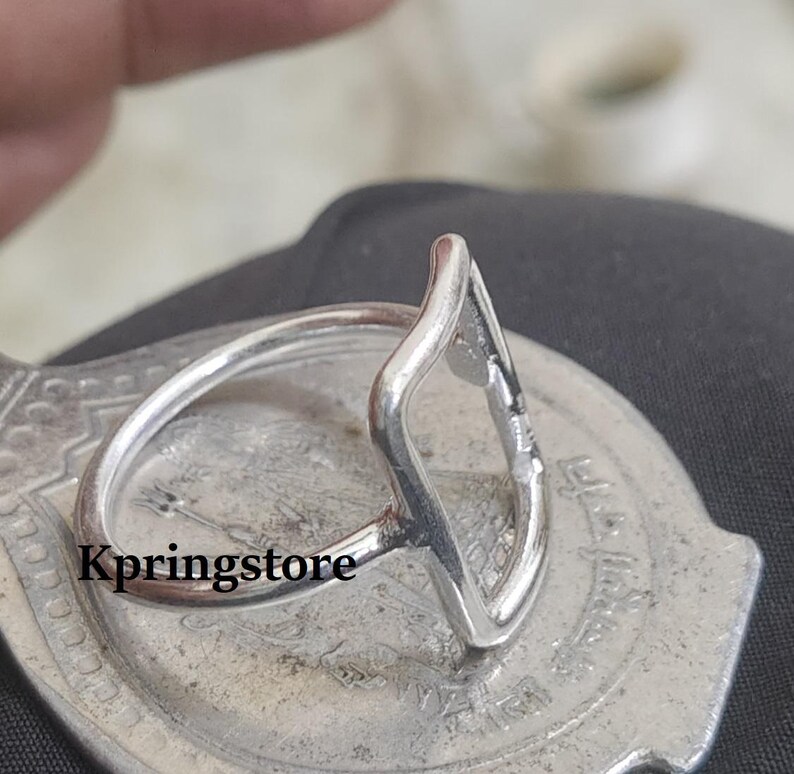 Peut inclure: Une bague en argent avec un design ouvert en forme de goutte d'eau. La bague est pos&eacute;e sur une surface argent&eacute;e textur&eacute;e. Le mot "Kpringstore" est imprim&eacute; sur la surface. L'anneau de la bague est fin et circulaire.