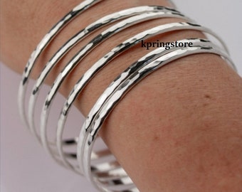 May include: Set of five silver hammered bangle bracelets. The bracelets are stacked on a person's wrist.