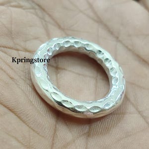 Puede incluir: Un anillo de plata con textura martillada. El anillo tiene forma ovalada y superficie texturizada. El anillo es una joya. El texto "Kpringstore" es visible en el lado izquierdo de la imagen.
