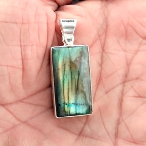 May include: A silver pendant featuring a rectangular green labradorite gemstone. The pendant has a silver bail.