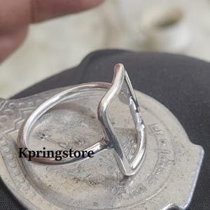 Peut inclure: Une bague en argent avec un design unique en forme de goutte d'eau ouverte. La bague est pos&eacute;e sur une surface argent&eacute;e textur&eacute;e, avec le mot "Kpringstore" visible. La bague a un anneau fin et circulaire, et la forme de goutte est ouverte au centre.