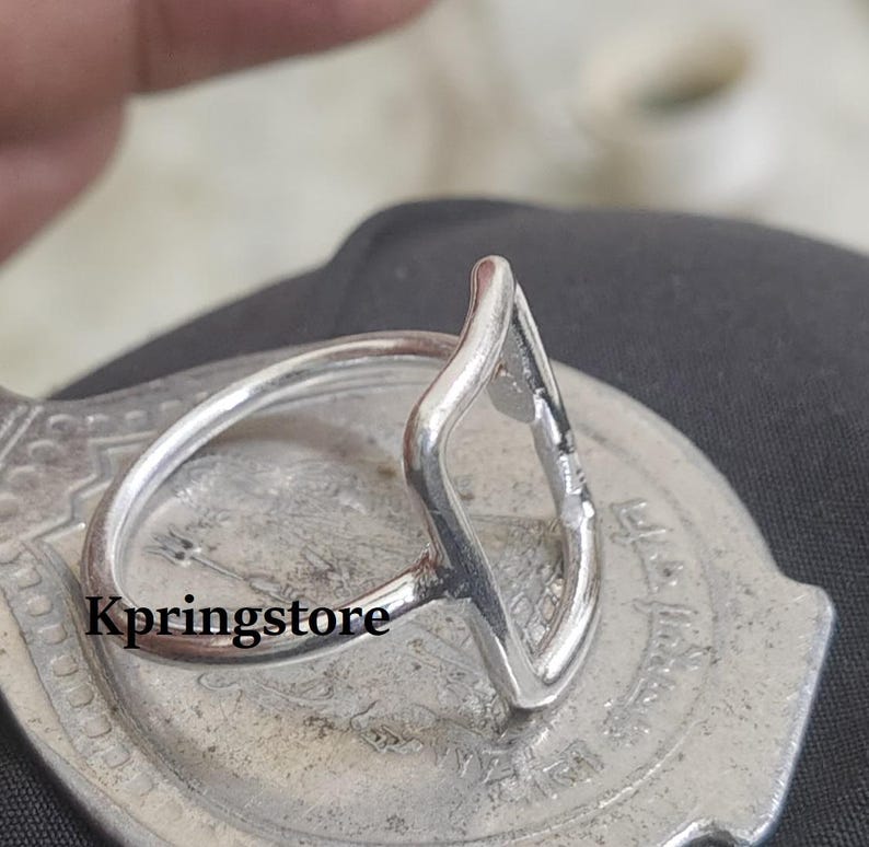 Peut inclure: Une bague en argent avec un design unique en forme de goutte d'eau ouverte. La bague est pos&eacute;e sur une surface argent&eacute;e textur&eacute;e, avec le mot "Kpringstore" visible. La bague a un anneau fin et circulaire, et la forme de goutte est ouverte au centre.