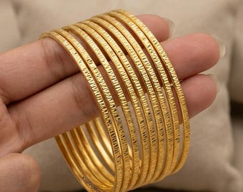 May include: A set of eight thin gold bangles featuring a textured, cross-hatched surface pattern. Each circular bracelet has a consistent metallic finish and a repeating etched design. The text Kspringstore is printed on the bottom-most bangle.