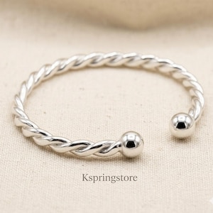 Peut inclure: Un bracelet manchette de couleur argentée présentant une texture torsadée semblable à une corde sur toute la bande et une perle sphérique lisse et polie à chaque extrémité ouverte. Le texte Kspringstore est imprimé sous le bracelet.