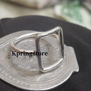 Peut inclure: Une bague argent&eacute;e avec un design rectangulaire. La bague est pos&eacute;e sur une surface argent&eacute;e avec le texte "Kpringstore". C'est un bijou minimaliste.
