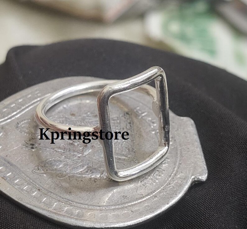 Peut inclure: Une bague argent&eacute;e avec un design rectangulaire. La bague est pos&eacute;e sur une surface argent&eacute;e avec le texte "Kpringstore". C'est un bijou minimaliste.