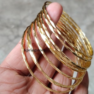 May include: A set of ten gold-toned bangles with a hammered finish. The bangles are stacked on top of each other and are arranged in a circular pattern.