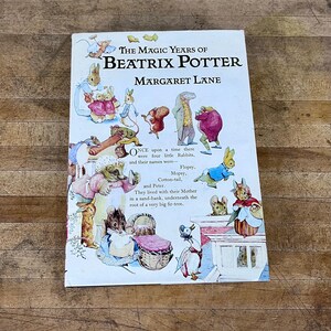 May include: A vintage book titled "The Magic Years of Beatrix Potter" by Margaret Lane. The cover features illustrations of rabbits and other animals in a colorful, whimsical style. The book is open, revealing text about the characters.
