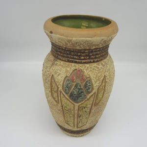 May include: A beige ceramic vase with a textured surface and a floral design. The vase has a brown band around the middle and a green interior. The floral design features pink, blue, and green accents.