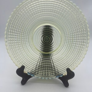 May include: A clear glass serving dish with a scalloped edge and a concentric circle pattern. The dish is on a black stand.