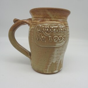 May include: A white ceramic mug with a black handle and the text "But First, Coffee" in a handwritten style. The mug is on a white surface. The mug is likely for hot beverages.