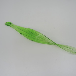 May include: A translucent, twisted glass sculpture in a vibrant green hue. The elongated form features a series of parallel lines, creating a textured effect. The piece has a rounded tip and a flared end, suggesting a decorative or artistic purpose.